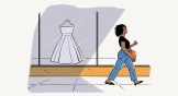 A woman walking by a store window with a wedding dress in it